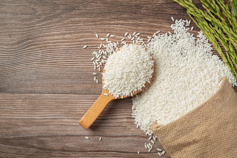 a sack of rice with rice on wooden spoon and rice plant